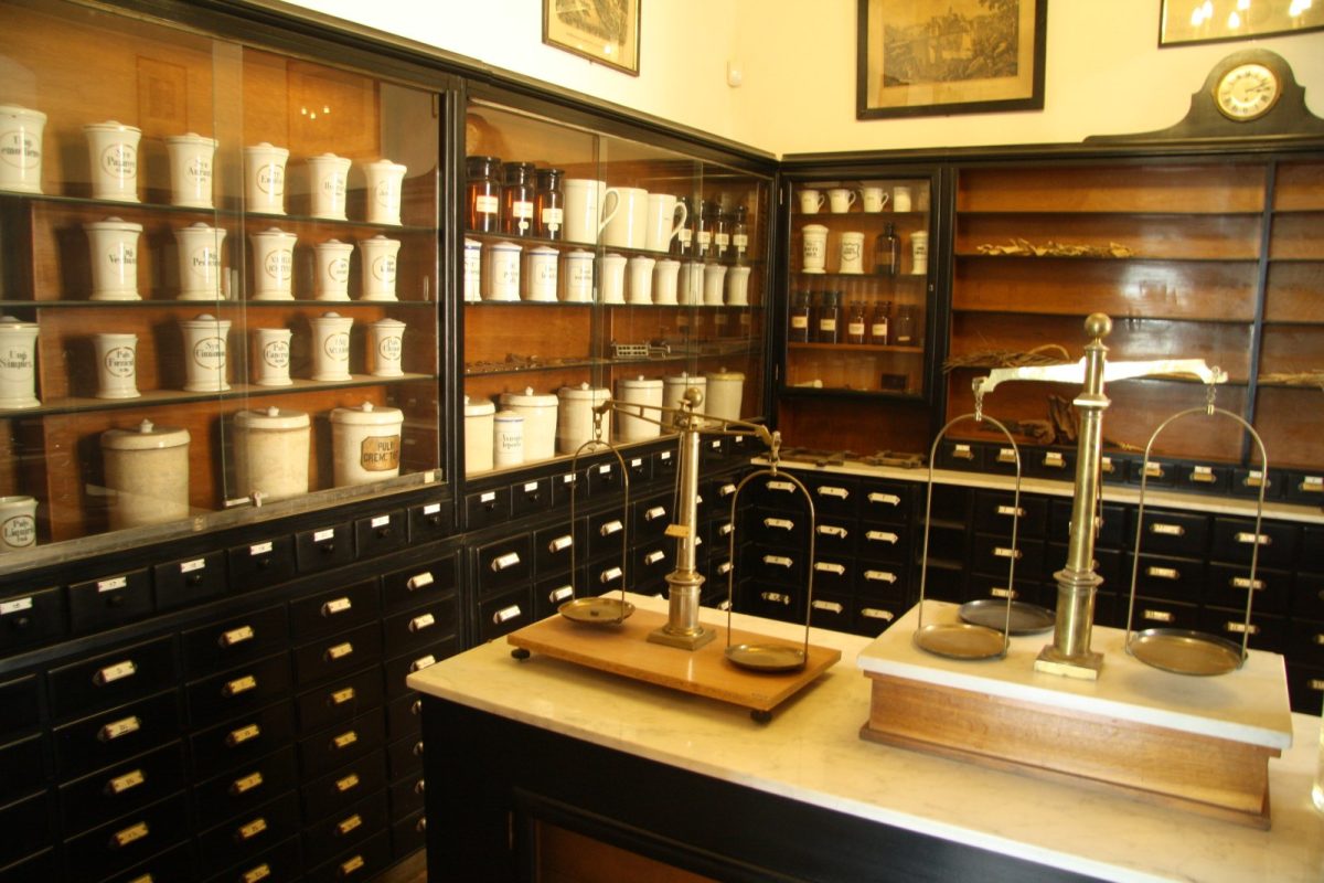 Interior de una farmacia antigua con botes de cerámica etiquetados, balanzas de precisión y cajones de madera