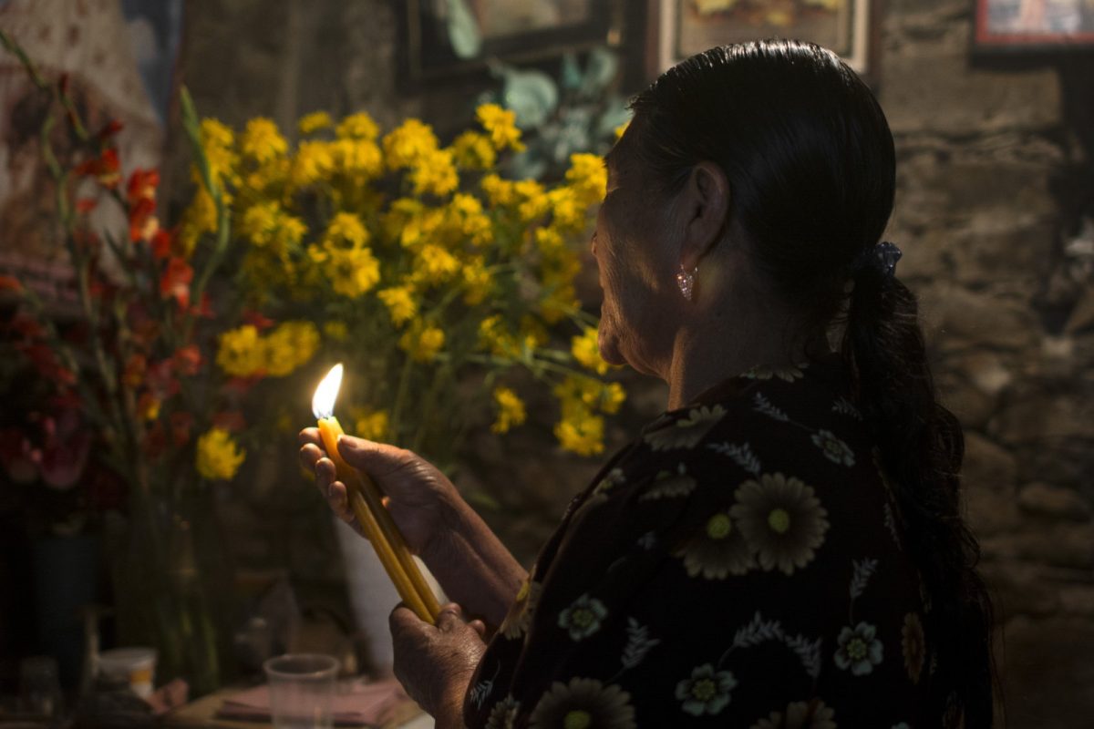 Curandera mazateca sostiene una vela encendida ante un altar con flores amarillas durante una limpia en Huautla de Jiménez, Oaxaca