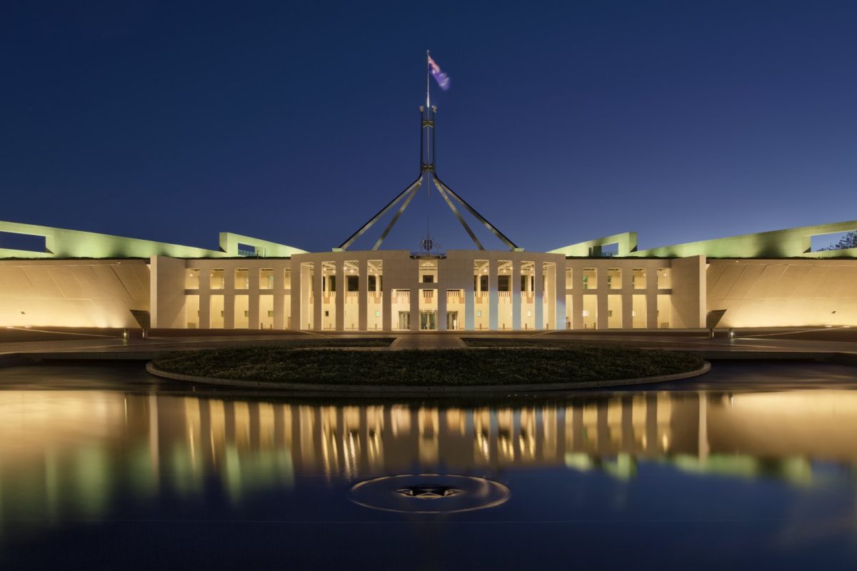 El edificio del Parlamento de Australia en Canberra iluminado al atardecer, reflejado en el agua.