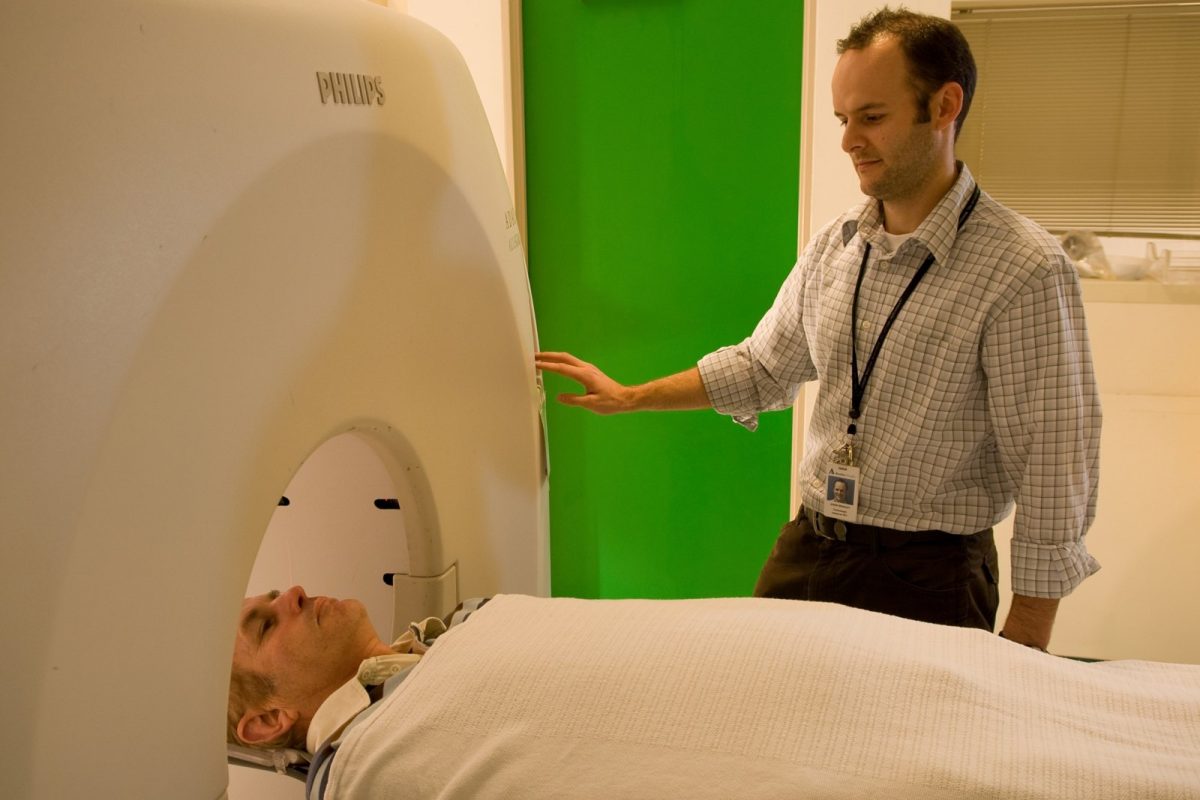 Una persona tumbada a punto de entrar en un escáner PET cerebral, con un técnico sanitario junto al equipo en una sala clínica.