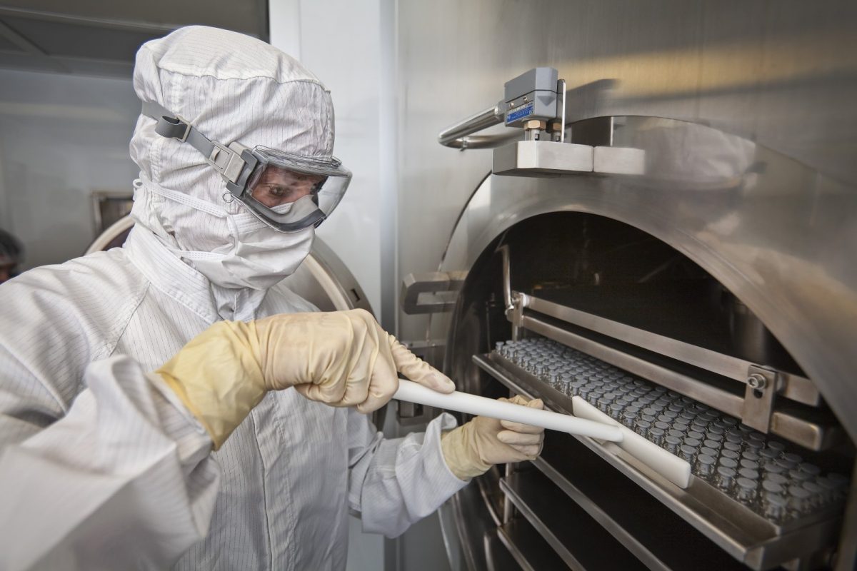 Técnico con traje completo de sala blanca introduciendo una bandeja de viales de vidrio en un liofilizador industrial de acero inoxidable