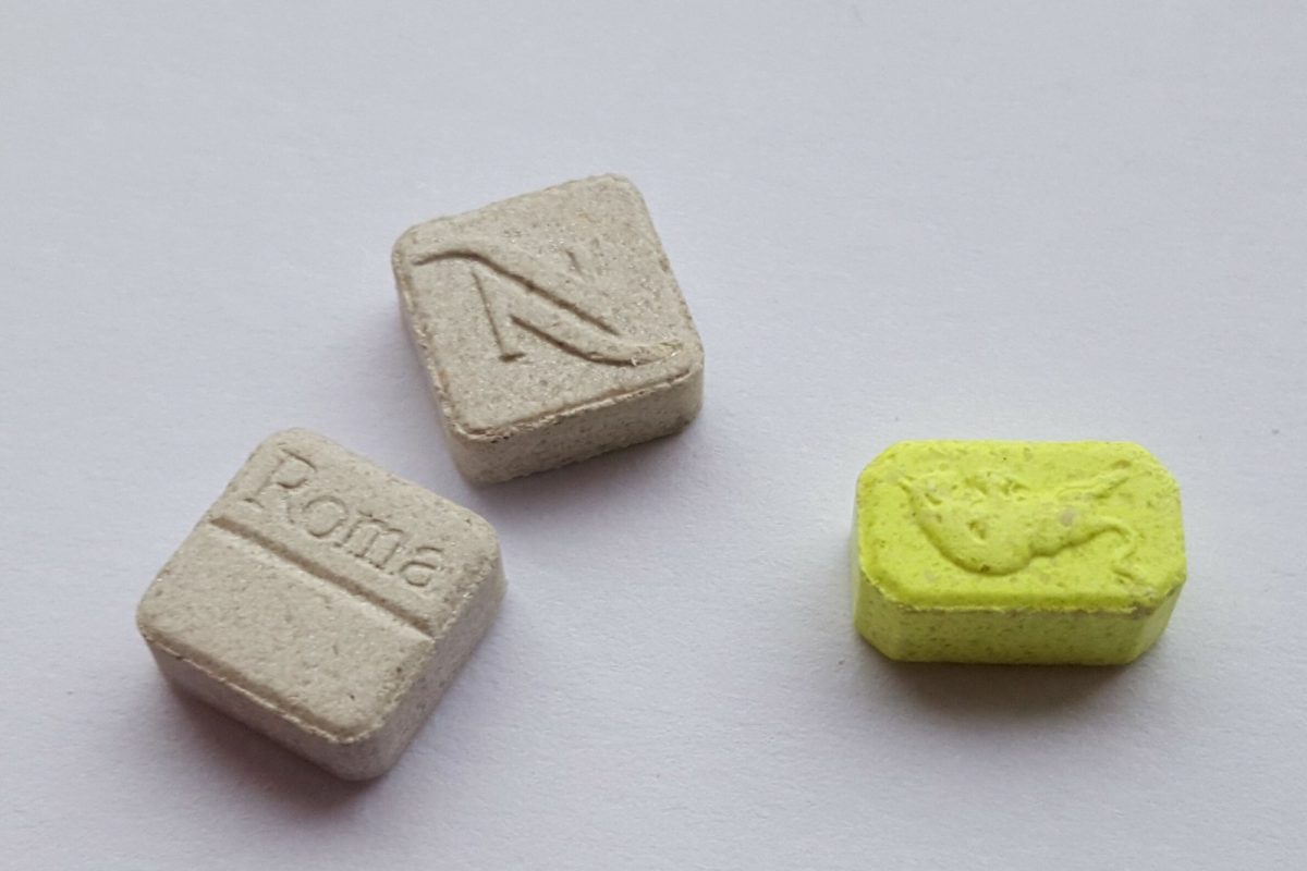 Tres comprimidos de MDMA con distintos logotipos grabados sobre un fondo claro y liso