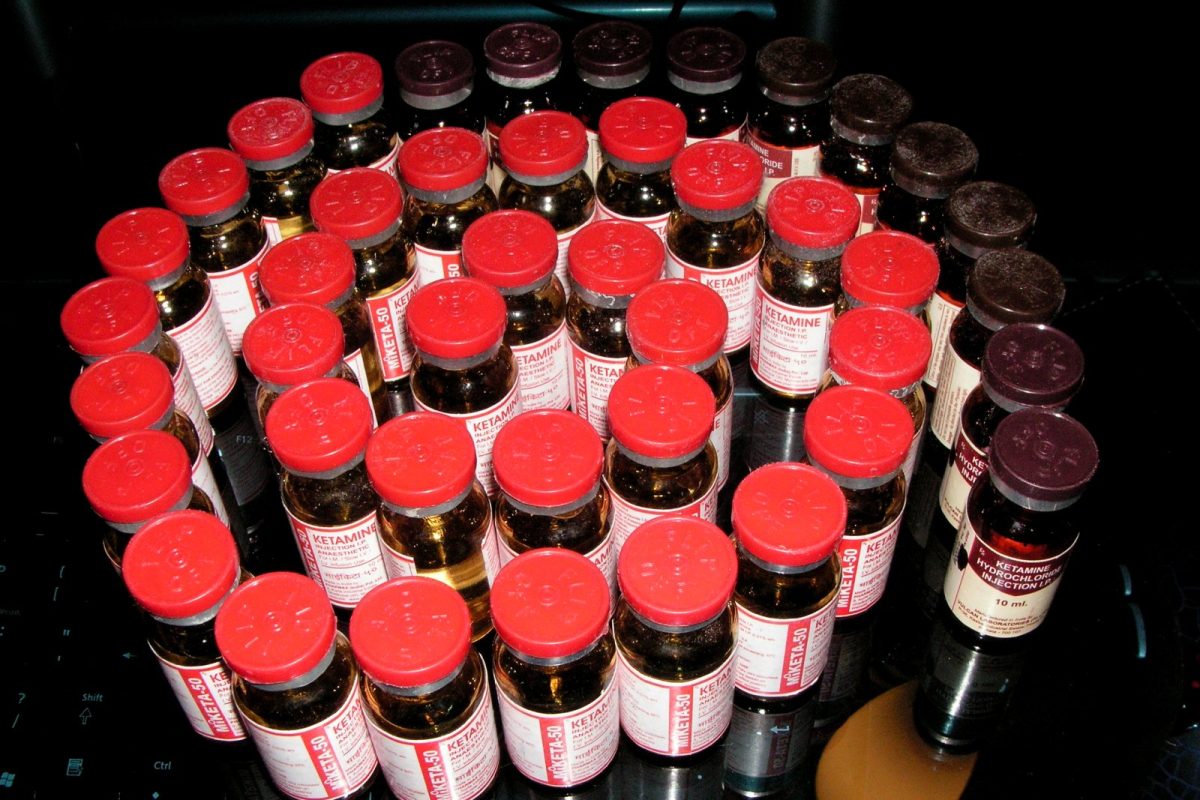 Viales de ketamina inyectable con tapón rojo y etiqueta farmacéutica, dispuestos sobre una superficie oscura