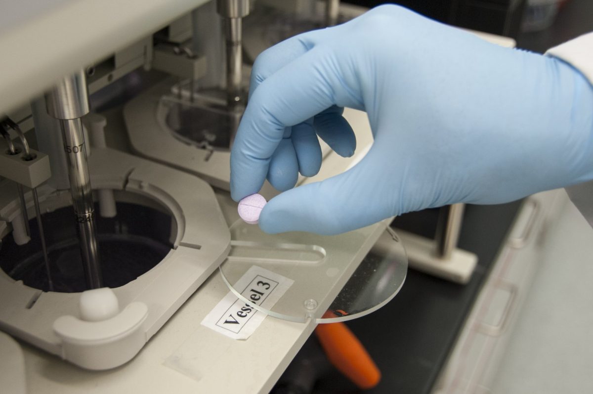 Investigador de laboratorio con guantes azules sostiene una tableta farmacéutica sobre un equipo de ensayo de disolución