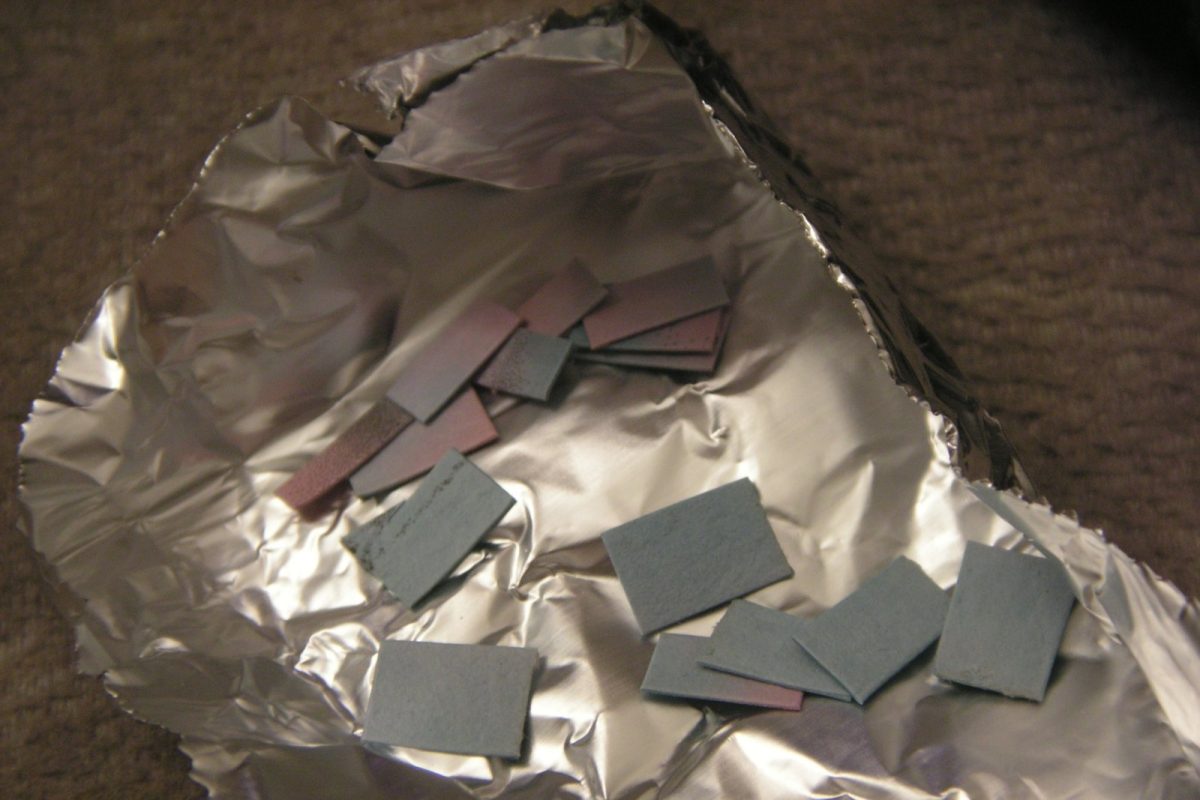 Varios cuadrados de papel secante de color azul y rosa esparcidos sobre una lámina de papel de aluminio