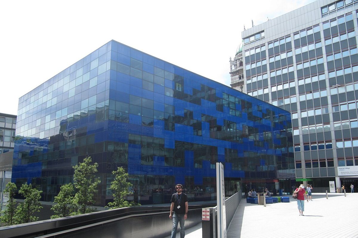 Edificio moderno de fachada acristalada azul del Imperial College de Londres, con gente caminando por la plaza peatonal.