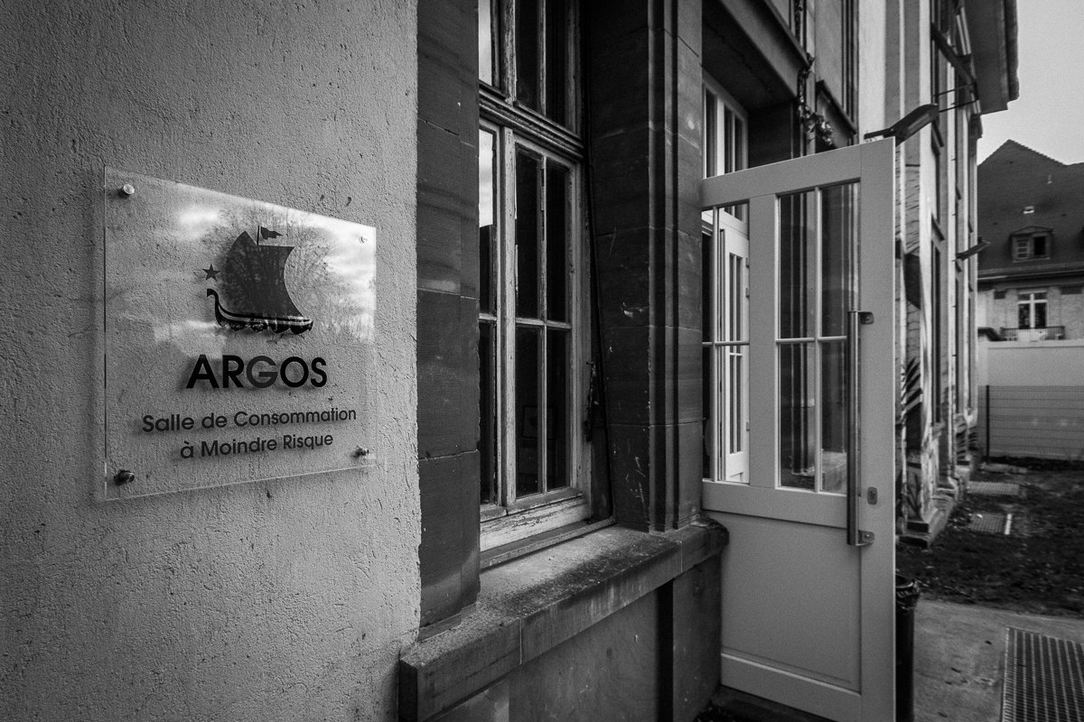 Placa junto a la puerta de un edificio con el texto ARGOS, Salle de Consommation à Moindre Risque, una sala de consumo supervisado en Estrasburgo.