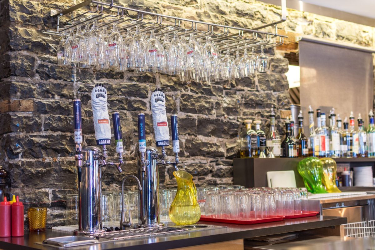 Barra de bar con tiradores de cerveza, copas colgadas y botellas al fondo