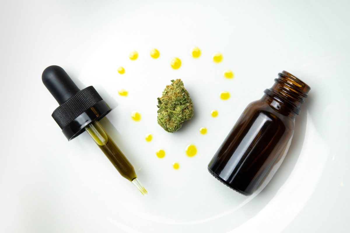 Frasco ámbar con cuentagotas, gotas de aceite y un cogollo de cannabis sobre un plato blanco