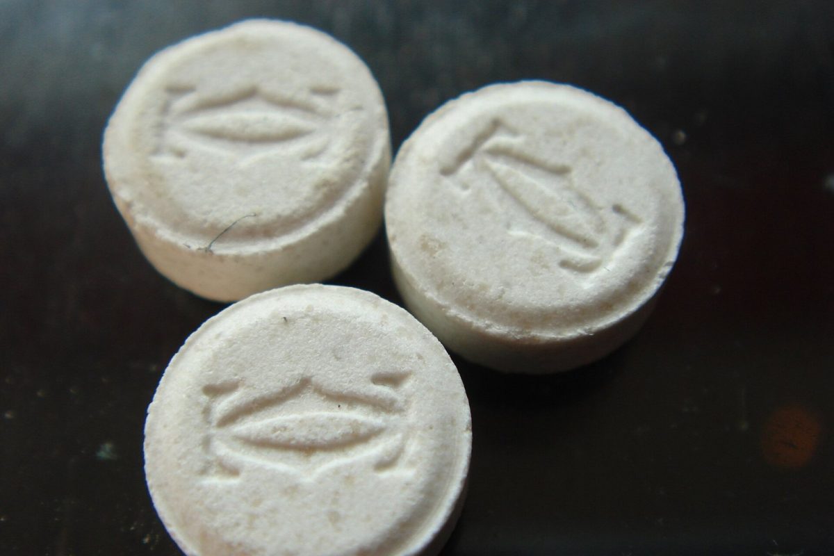 Tres pastillas blancas prensadas con un logotipo grabado en relieve, vistas de cerca sobre una superficie oscura