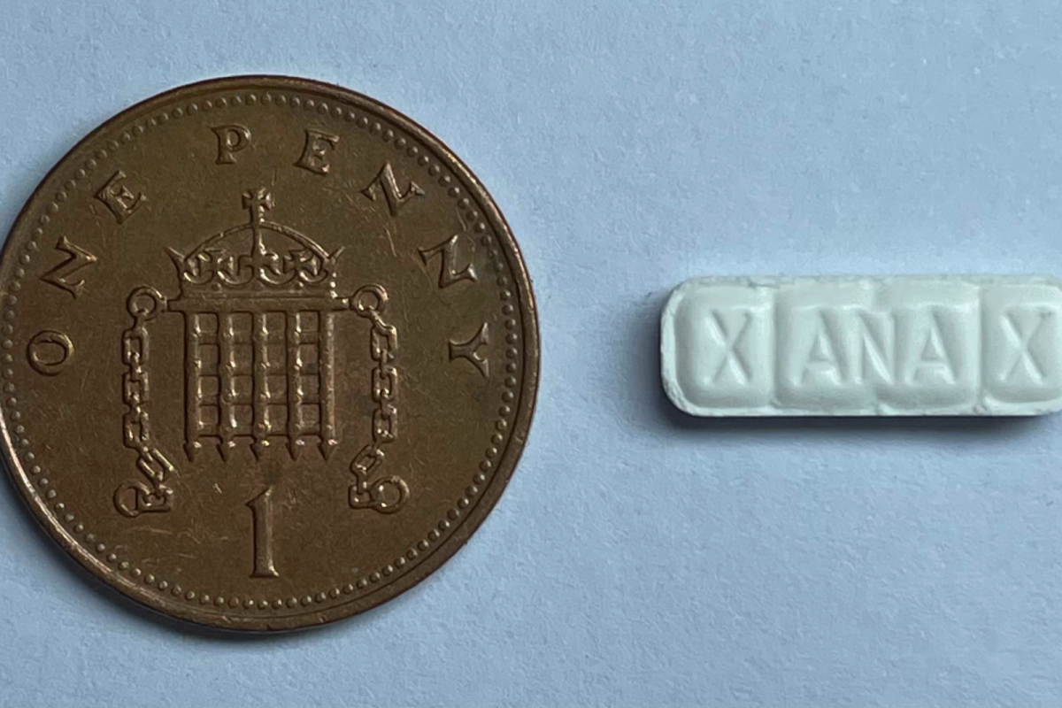 Pastilla rectangular blanca grabada con la palabra XANAX, junto a una moneda de un penique que sirve de escala