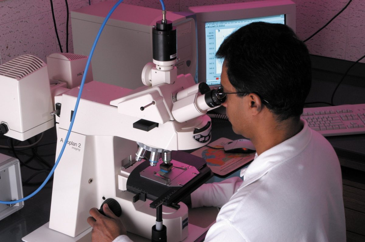 Investigador con bata blanca observa una muestra por los oculares de un microscopio de laboratorio