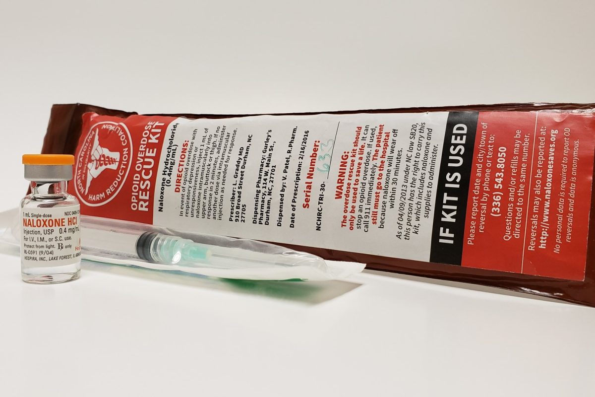 Vial de naloxona de 0,4 mg/ml junto a una jeringa estéril precintada y el envase rojo de un kit de rescate ante sobredosis por opioides, sobre fondo blanco.