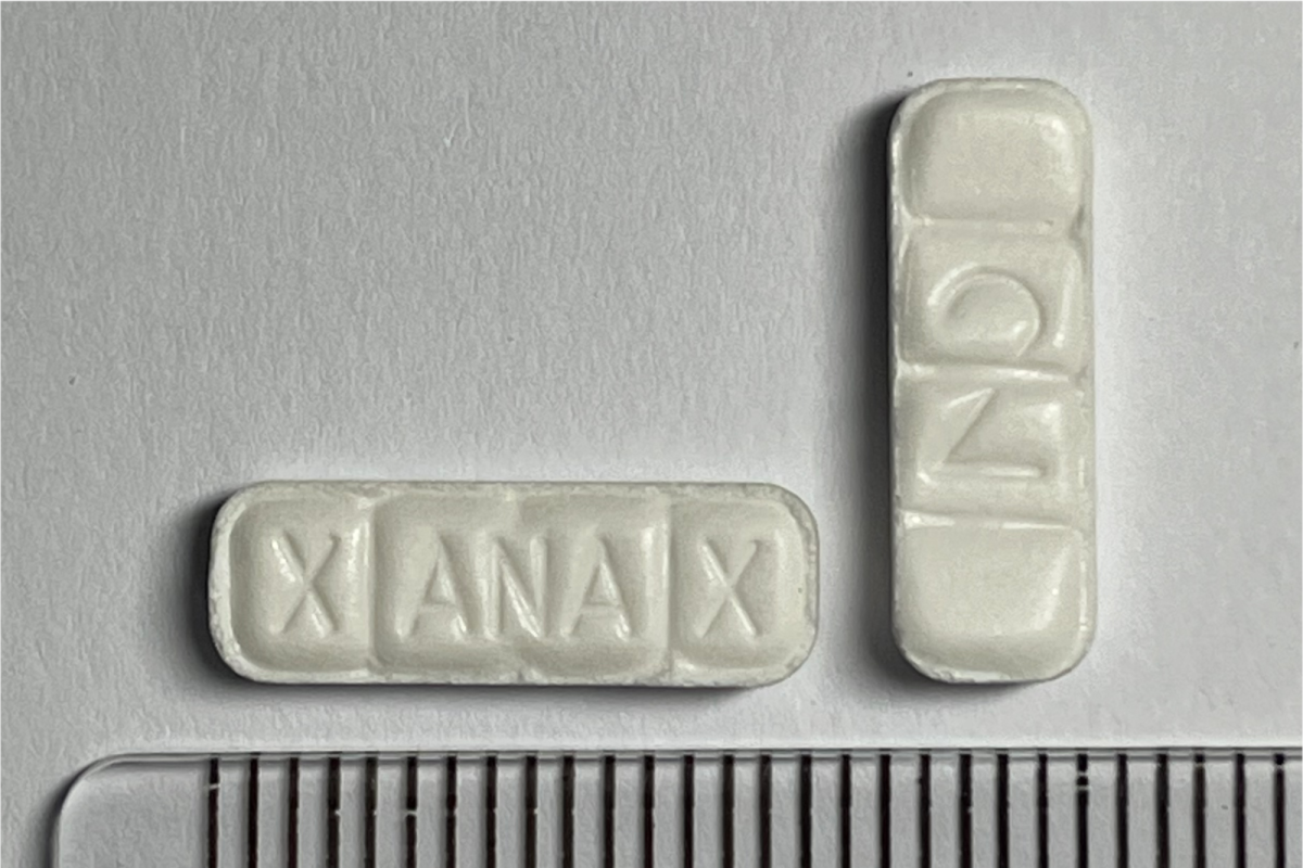 Dos comprimidos blancos falsificados marcados XANAX y ONZ junto a una regla graduada en centímetros sobre fondo gris