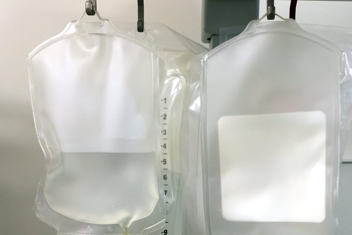 Dos bolsas de suero intravenoso colgadas de un soporte en una sala clínica, sin ningún nombre de medicamento visible