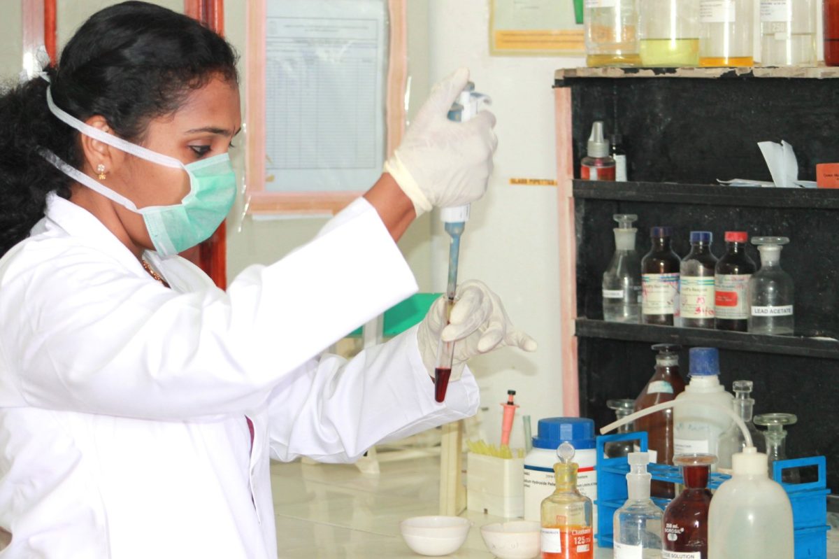 Técnica de laboratorio con mascarilla y guantes pipeteando una muestra en un laboratorio de toxicología
