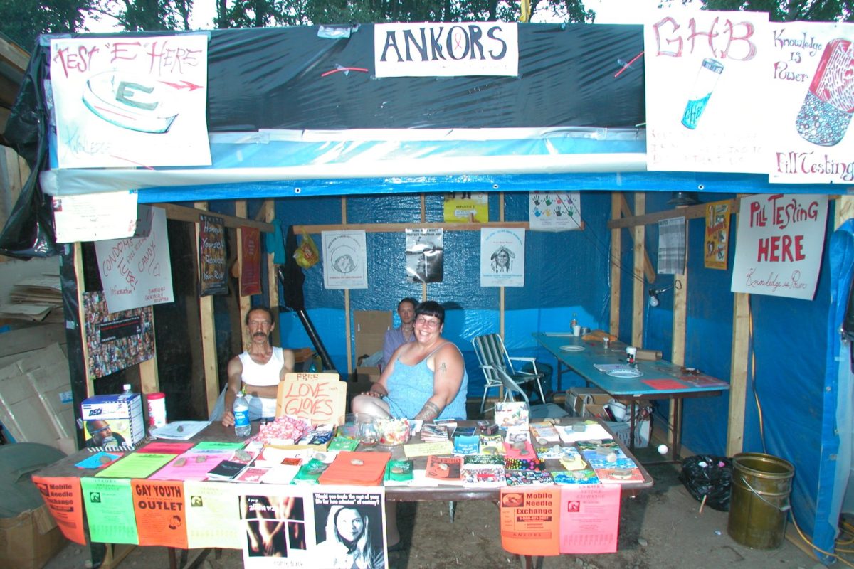 Carpa de reducción de riesgos en un festival con carteles de análisis de pastillas y una mesa llena de folletos informativos