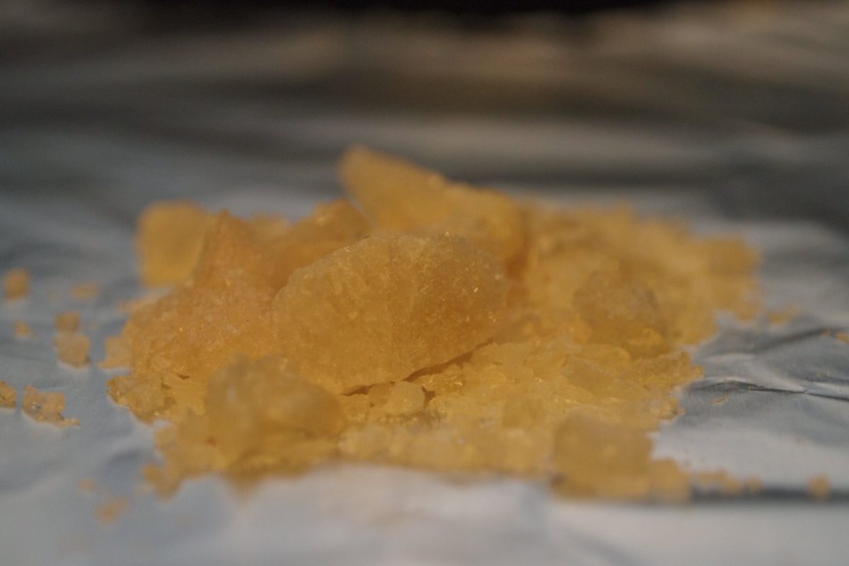 Primer plano de cristales de MDMA de color ámbar sobre una lámina de aluminio, con enfoque muy poco profundo.