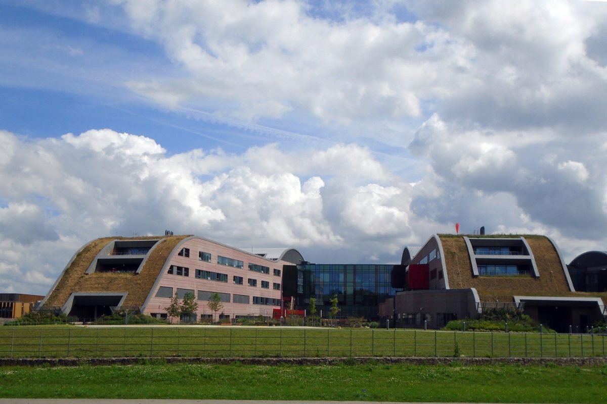 Edificio del hospital infantil Alder Hey en Liverpool, con cubiertas verdes onduladas, visto desde un parque bajo un cielo con nubes