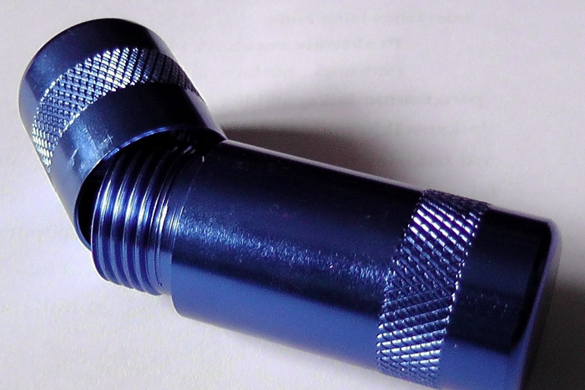 Dispositivo metálico azul con rosca y zona estriada usado para abrir cartuchos de óxido nitroso, sobre fondo claro