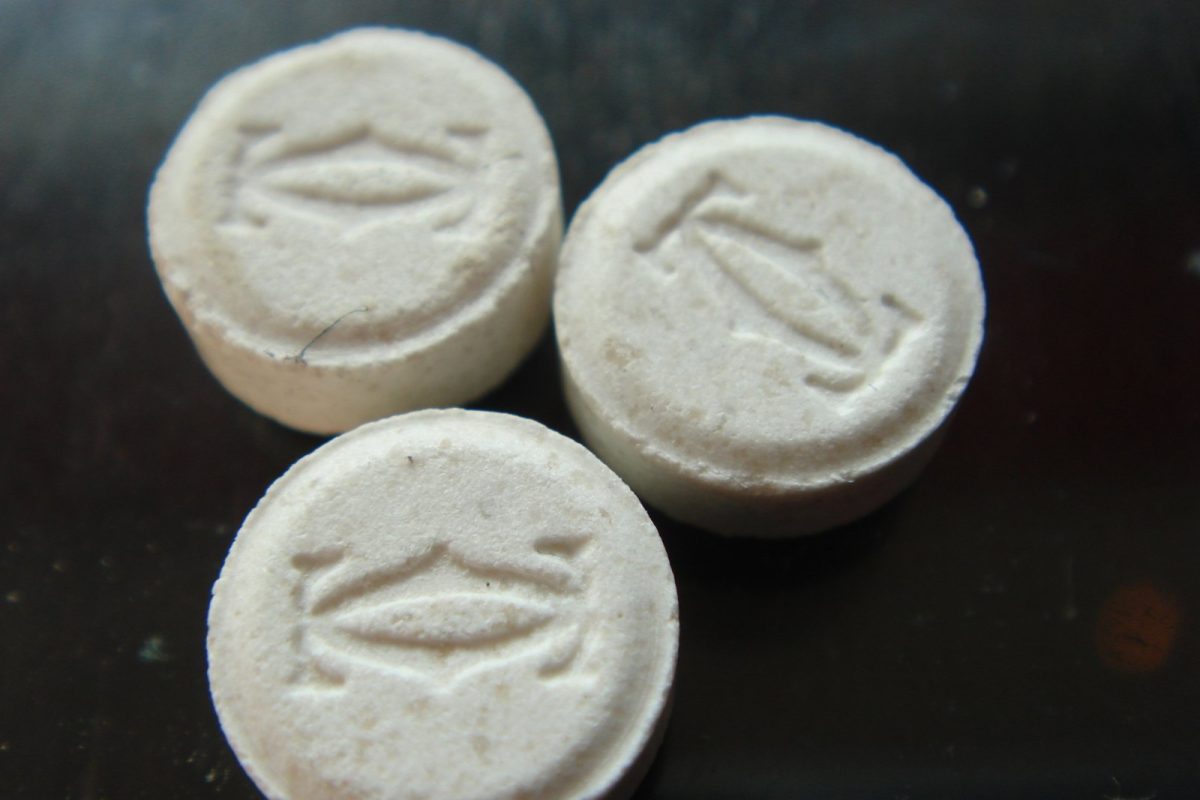 Tres pastillas blancas de éxtasis (MDMA) con relieve grabado, sobre una superficie oscura